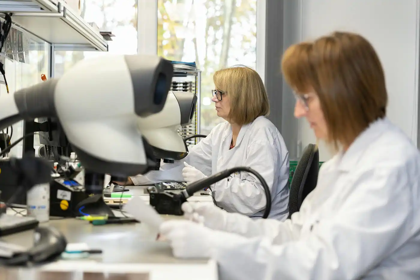 Mitarbeiterinnen führen die Detailkontrolle an Stereomikroskopen durch