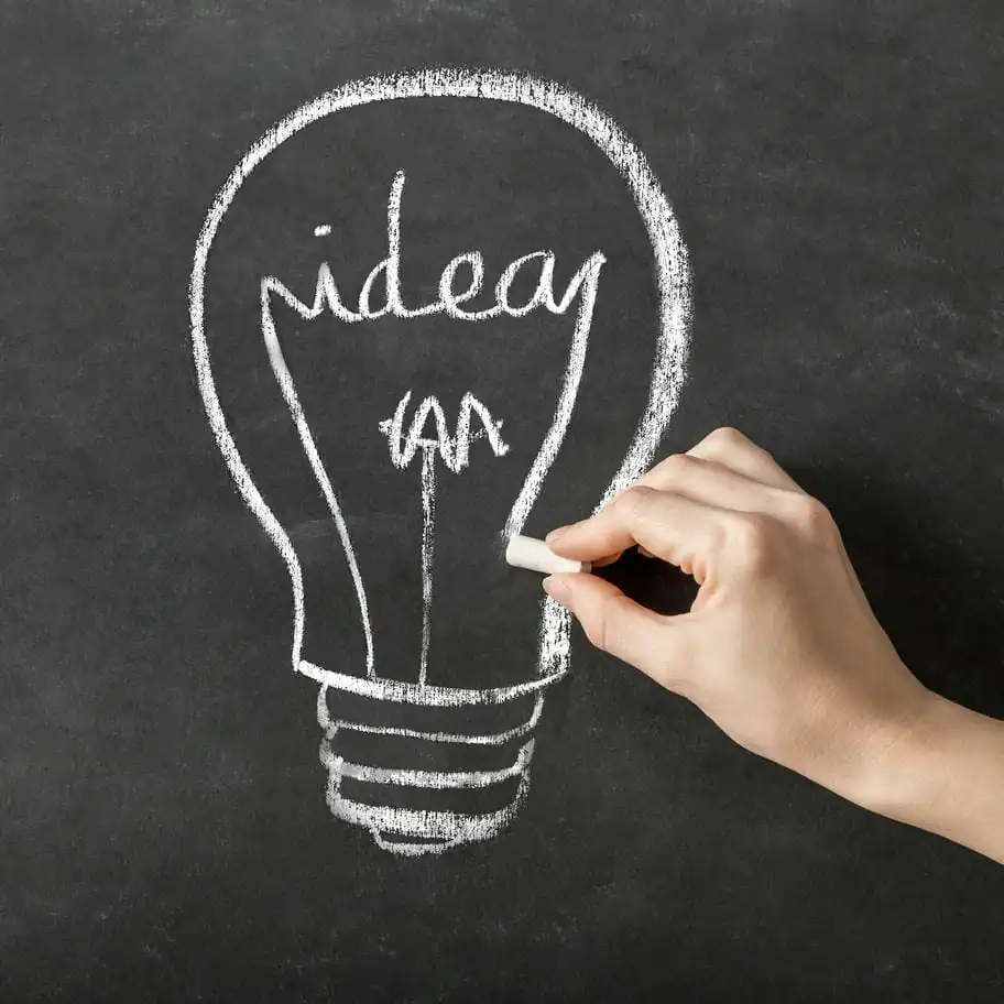 Eine Hand hat eine Glühbirne mit dem Schriftzug "idea" auf eine Kreidetafel gezeichnet